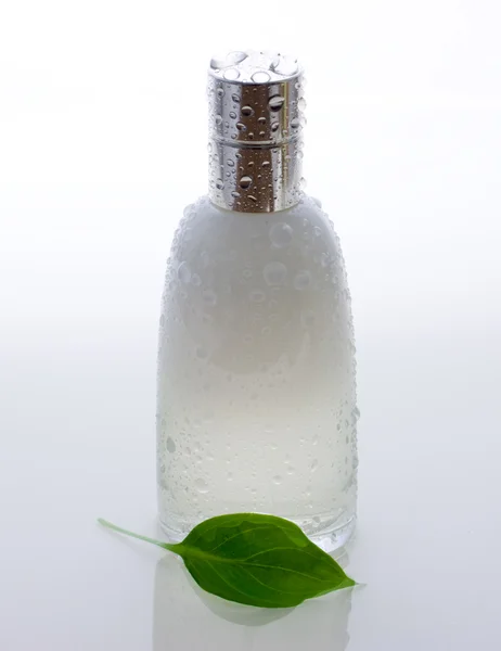 Perfume bottle and green leaf with drops