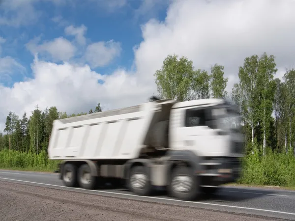 White dump truck speeding on rural highway, motion blur