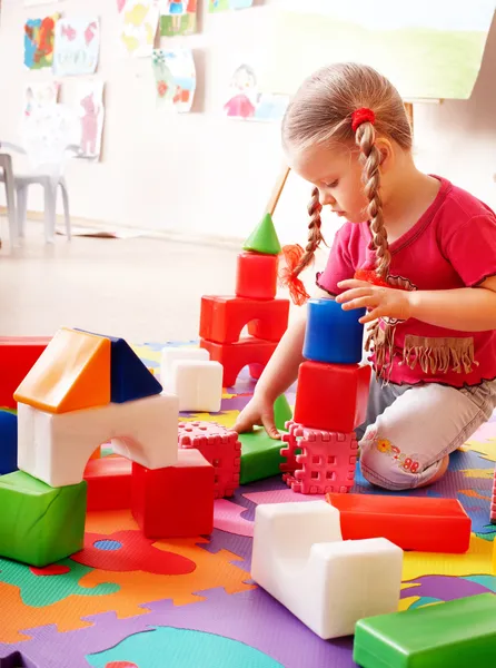 Child with puzzle, block and construction set in play room.