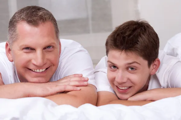 Friendly father and son smiling and lying on the bed