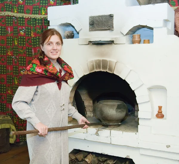 Woman puts a pot into russian stove