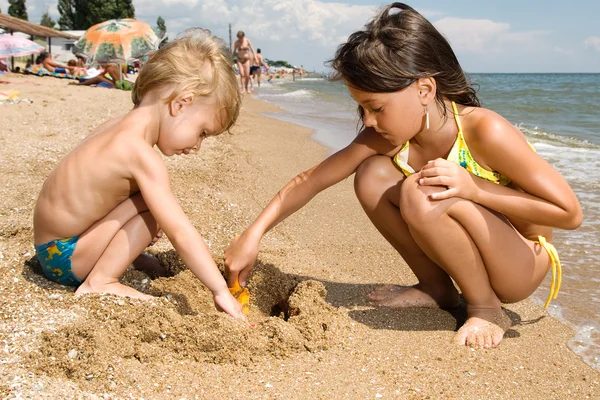 Two young kids digging sand at the beach