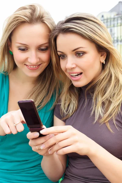 Two smiling girls watching something in mobile phone