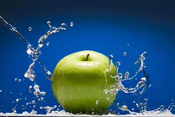 Green apple with water splash on blue background