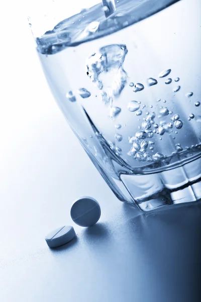 Aspirin pills and glass of water toned blue