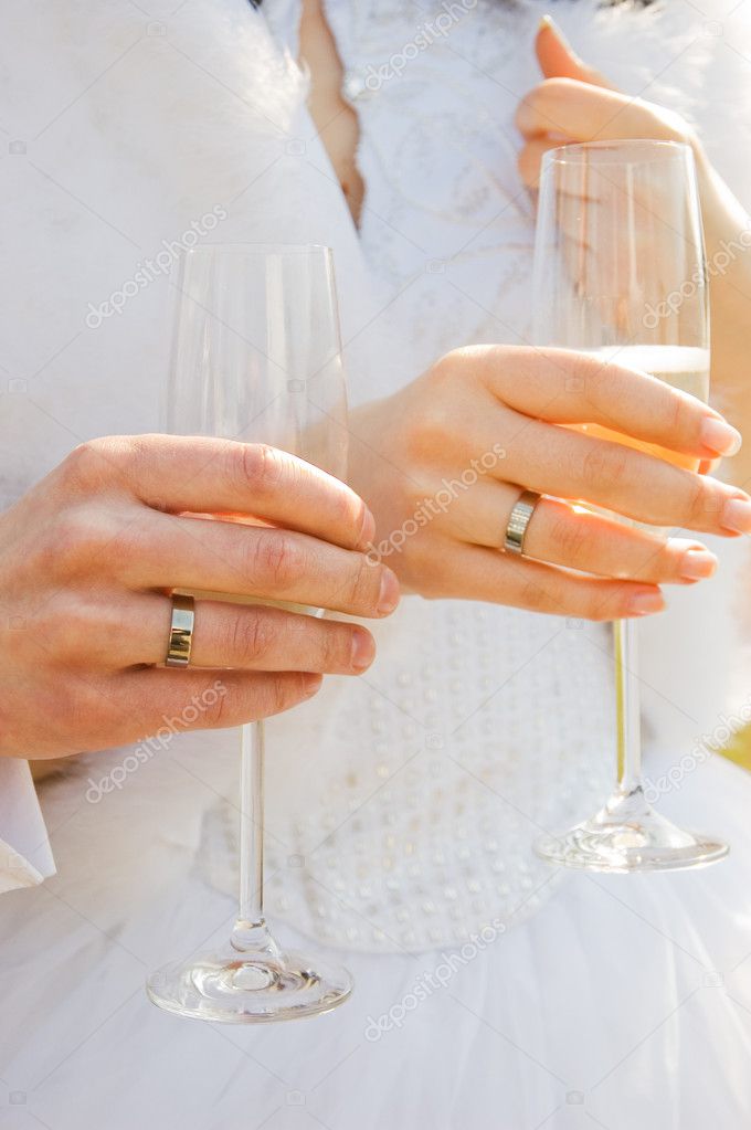 Two hands with wedding rings holding champagne glasses