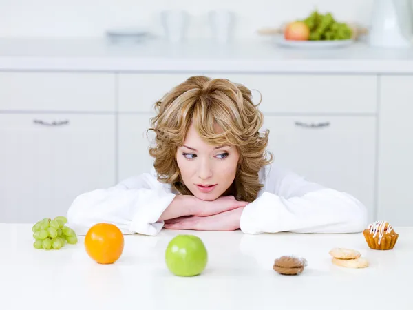 Woman choosing between fruits and cakes