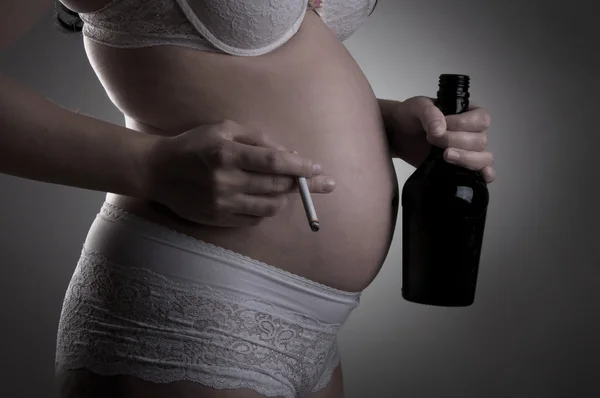 A pregnant woman with bottle of alcohol and cigarette