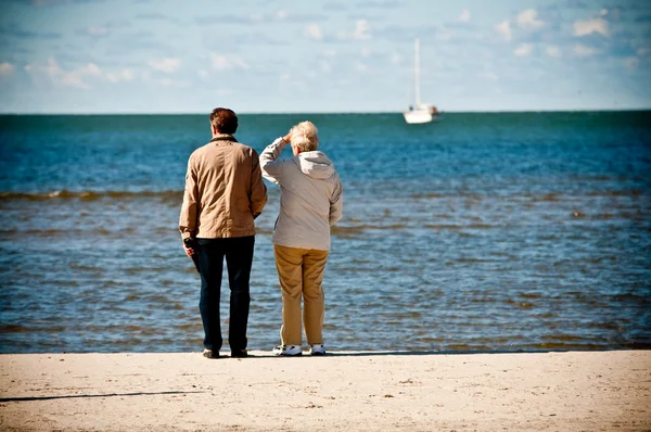 Elderly couple on seashore looking boat at the sea