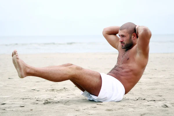 Attractive and happy man training abs on beach