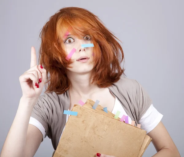 Red-haired student with book and notes on face.