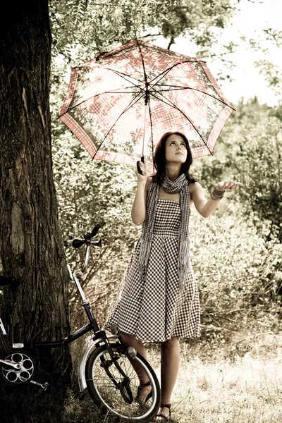 Beautiful girl near bike and tree at rest in forest. Photo in retro