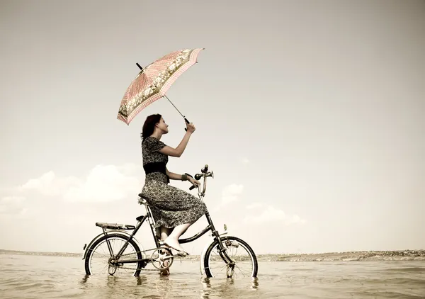Girl go for a cycle ride at water with umbrella in hand. Photo in retro sty