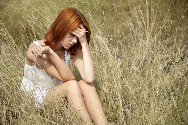 Sad red-haired girl at grass.