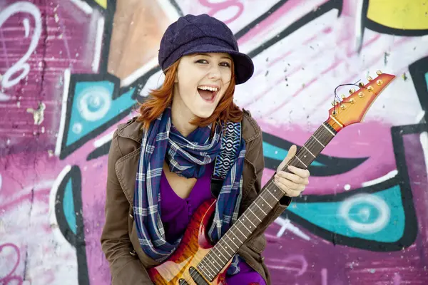 Closeup portrait of a happy young girl with guitar and graffiti