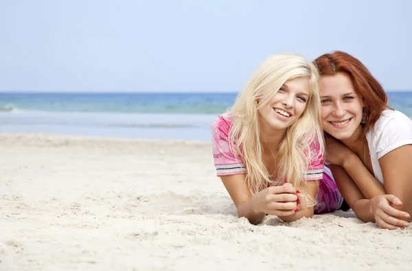 Two girl friends lying down at the beach.