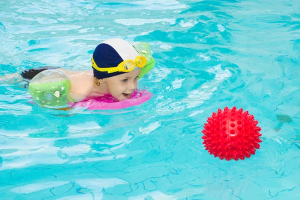 Child in swimming pool, kid swim playing water ball, boy indoor training