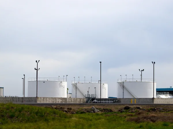 White fuel tanks in a field with an overcast sky