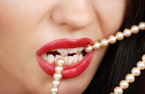 Woman biting pearl necklace with red lipstick
