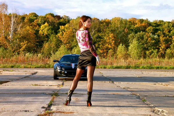 Seductive young woman in shot skirt near sport car. Nature.