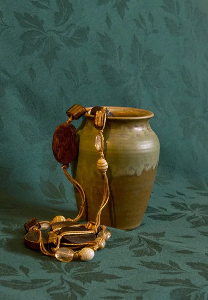 Ceramic jar and necklace on green background — Stock Photo, Image