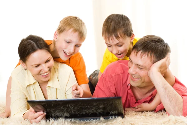 Familia acostada en la alfombra con un portátil — Foto de Stock