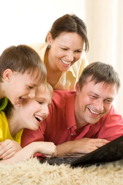 Familjen ligger på mattan med en bärbar dator — Stockfoto