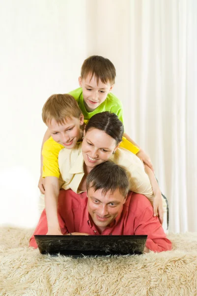 Família deitada no tapete com um laptop — Fotografia de Stock