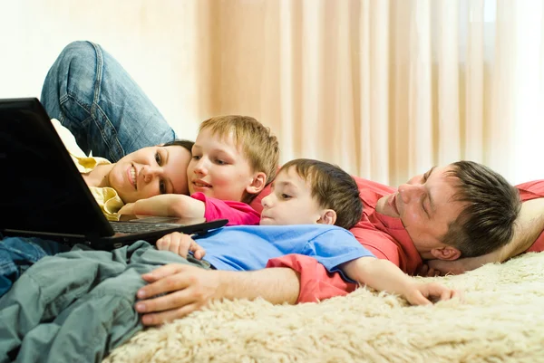 Семья лежит на ковре с ноутбуком — стоковое фото