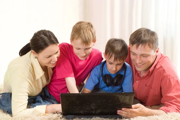 Familia acostada en la alfombra con un portátil — Foto de Stock