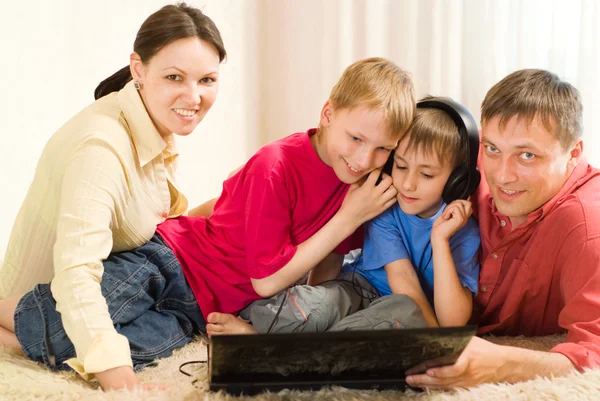 Familjen ligger på mattan med en bärbar dator — Stockfoto
