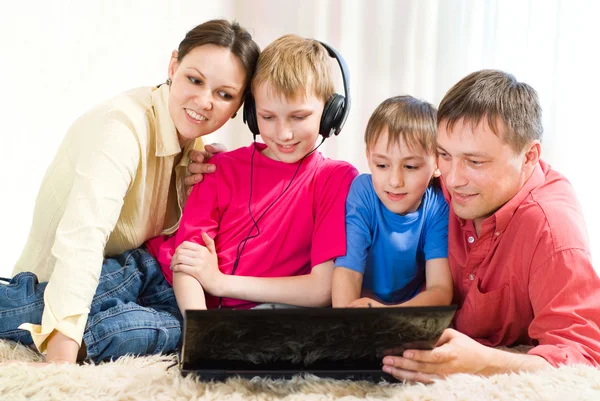 Bir dizüstü bilgisayar ile halının üzerinde yalan aile — Stok fotoğraf