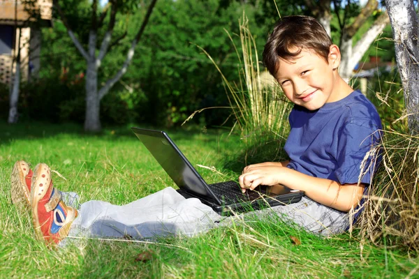 Chłopiec z notebooka siedzieć w drzewo na zewnątrz — Zdjęcie stockowe