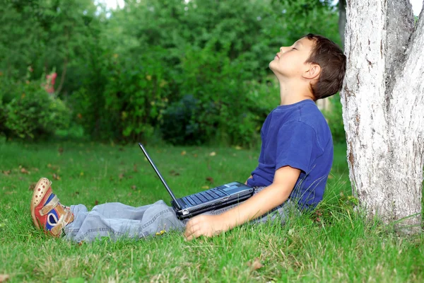 Chłopiec z notebooka siedzieć w drzewo na zewnątrz — Zdjęcie stockowe