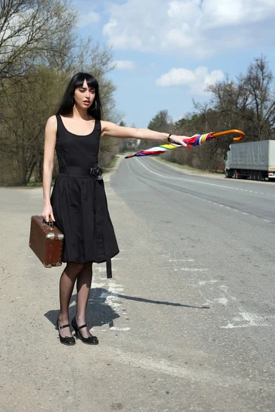 Автостопом девушка с винтажным чемоданом — стоковое фото