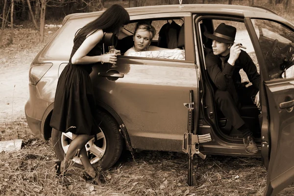 Две девушки, машина и мужчина с винтовкой — стоковое фото