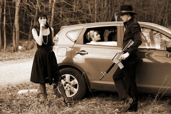 Две девушки, машина и мужчина с винтовкой — стоковое фото