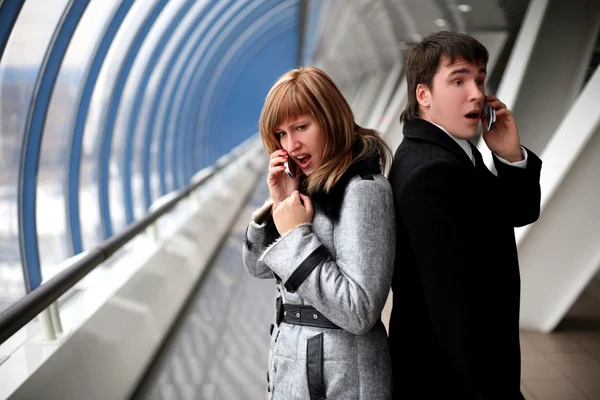 Man and woman speaking phones inside bridge