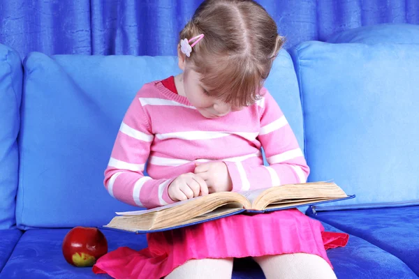 Menina livro de leitura com maçã no sofá — Fotografia de Stock