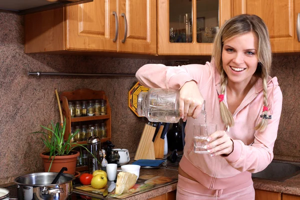 Donna che cucina la cena e tenendo il bicchiere con acqua limpida nel k — Foto Stock