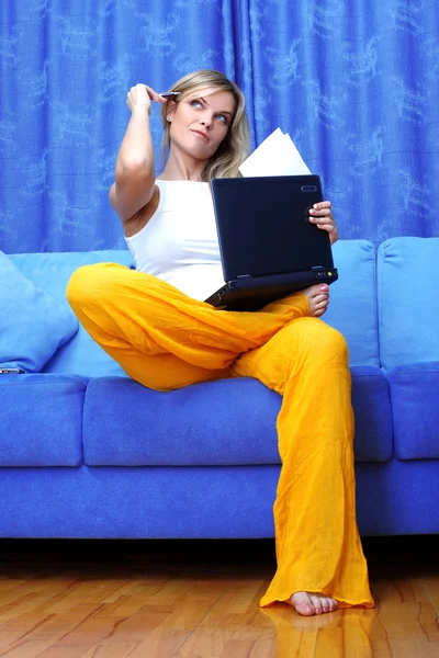Мыслительная женщина, работающая с компьютером дома на диване — стоковое фото