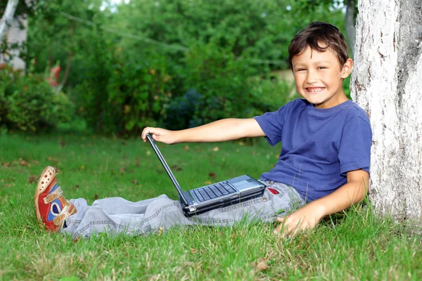 Garçon avec ordinateur portable assis à l'arbre à l'extérieur — Photo