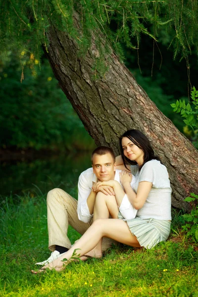 Jovem casal sentado debaixo da árvore — Fotografia de Stock