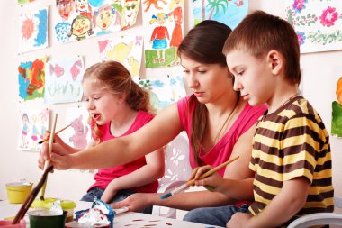 Child with teacher draw paints in play room. clipart