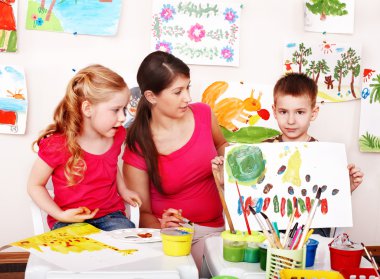 Child with teacher draw paints in play room. clipart