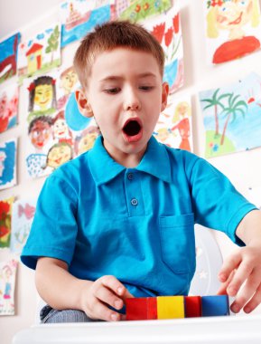 Child with wood block and construction set in play room. clipart