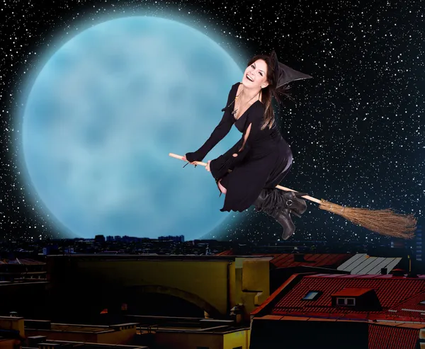 Dívka čarodějnice létají nad městem proti měsíc a hvězdné oblohy. — Stock fotografie