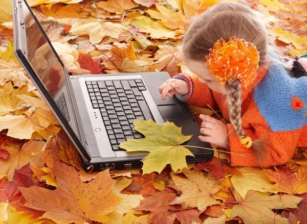 Bambino in autunno foglie arancioni con computer portatile . — Foto Stock