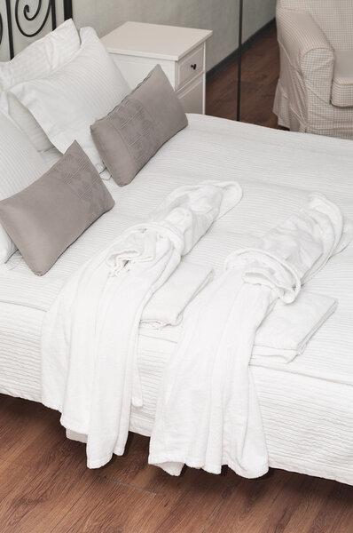 Two terry white dressing gowns on bed