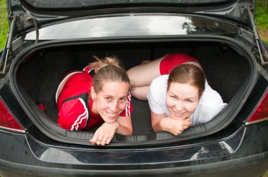 Two young women in car boot happy and smiling clipart